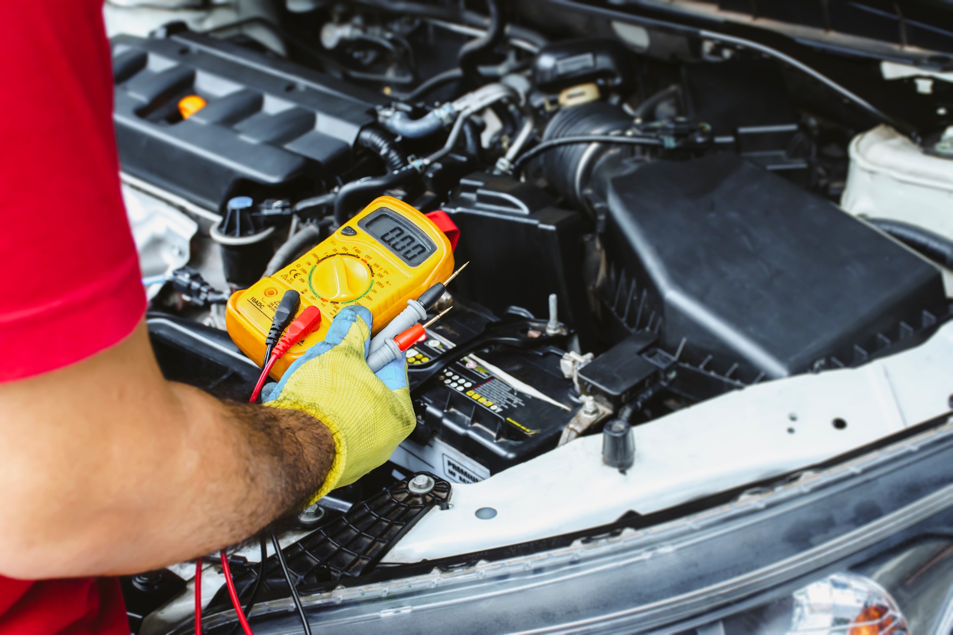 A mechanic holds a digital multimeter to check the car electrical system